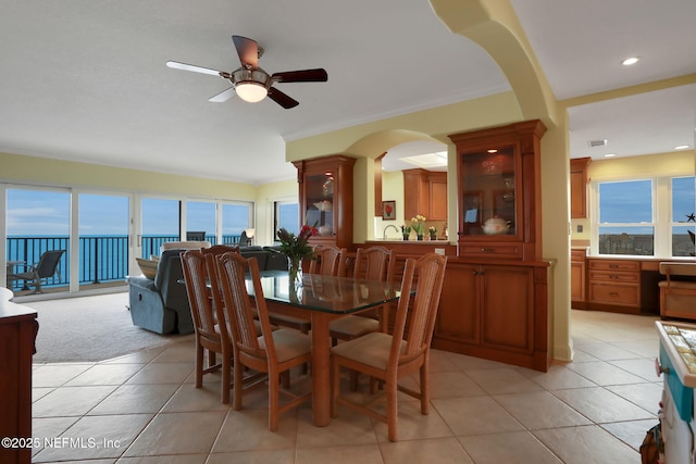 dining space with light tile patterned floors, a water view, a ceiling fan, and crown molding