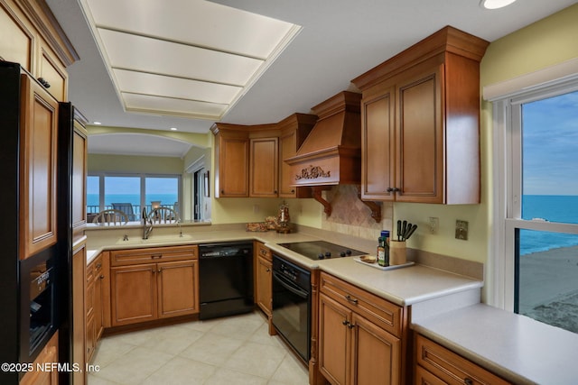 kitchen featuring a water view, light countertops, black appliances, premium range hood, and a sink