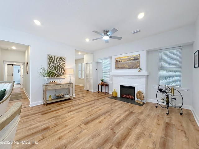 living area with recessed lighting, a fireplace with flush hearth, a healthy amount of sunlight, light wood-type flooring, and baseboards