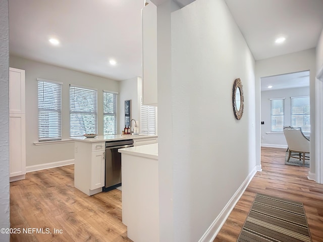 kitchen with a peninsula, white cabinets, light countertops, dishwasher, and light wood finished floors