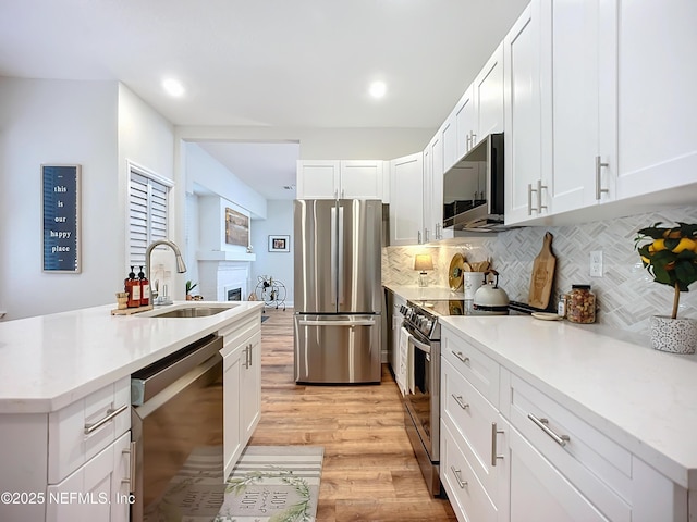 kitchen featuring white cabinets, appliances with stainless steel finishes, light countertops, light wood-type flooring, and a sink