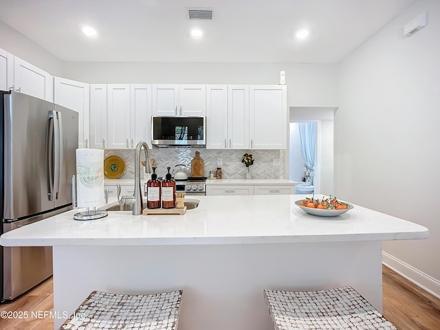 kitchen featuring a center island with sink, visible vents, stainless steel appliances, light countertops, and white cabinetry