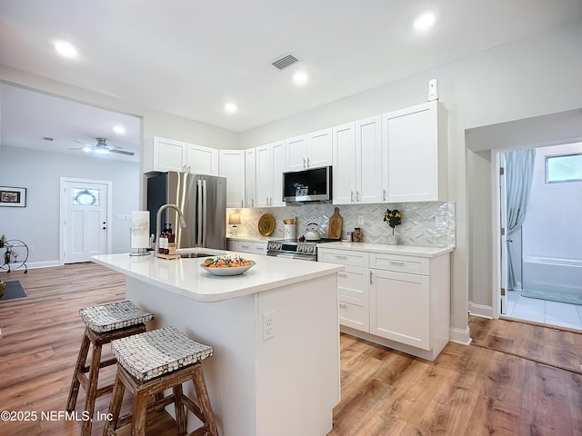 kitchen featuring stainless steel appliances, an island with sink, visible vents, and white cabinets