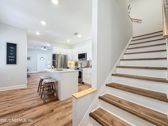 kitchen featuring a center island with sink, white cabinets, a breakfast bar area, stainless steel appliances, and light countertops