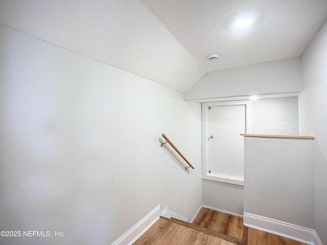 stairway featuring vaulted ceiling, a textured ceiling, baseboards, and wood finished floors