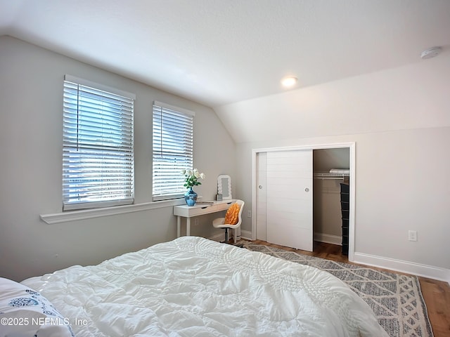 bedroom featuring lofted ceiling, a closet, wood finished floors, and baseboards