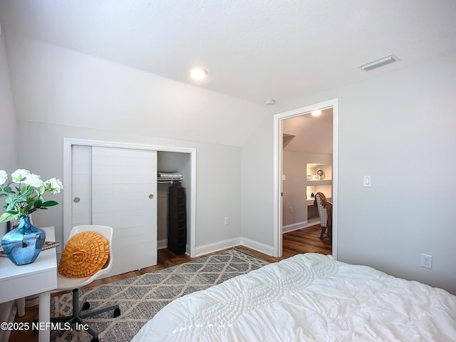 bedroom with dark wood finished floors, visible vents, vaulted ceiling, and a closet