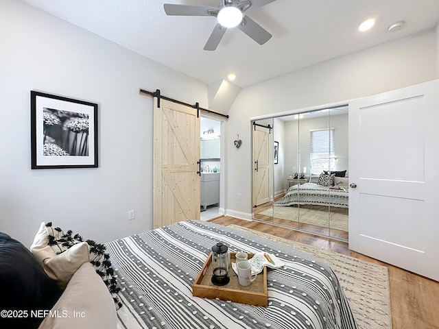 bedroom with ensuite bathroom, a barn door, light wood-style flooring, recessed lighting, and a closet