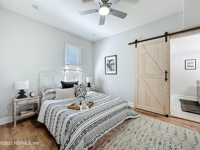 bedroom featuring a barn door, wood finished floors, a ceiling fan, and baseboards