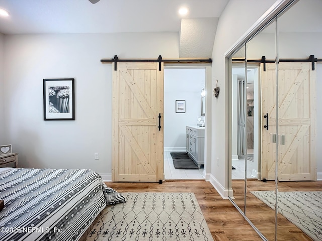 bedroom with a barn door, a closet, wood finished floors, and baseboards