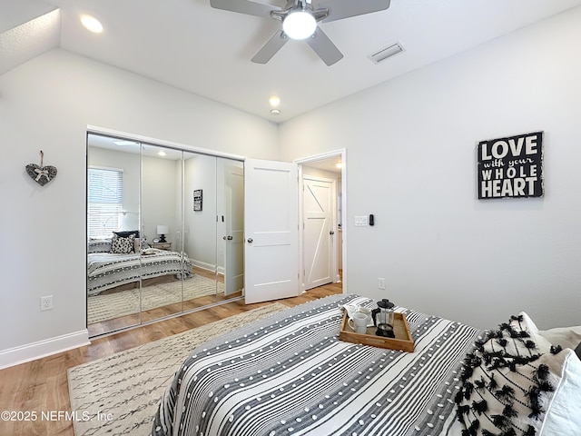 bedroom with lofted ceiling, wood finished floors, visible vents, baseboards, and a closet