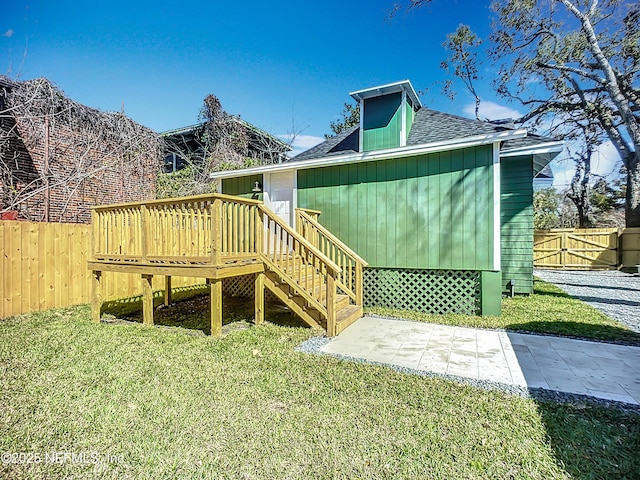 rear view of property featuring roof with shingles, a patio area, fence, and a lawn