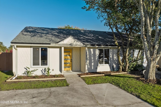 view of front of house with a shingled roof, a front lawn, and fence