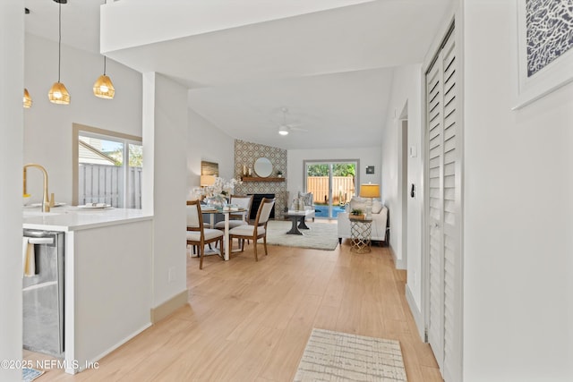 corridor featuring light wood-style flooring, beverage cooler, a sink, baseboards, and vaulted ceiling