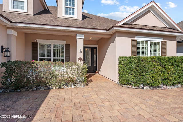 property entrance featuring stucco siding and a shingled roof