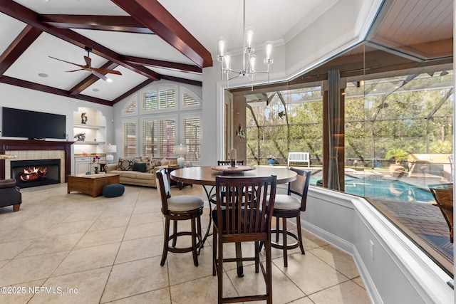 dining area with a tiled fireplace, light tile patterned flooring, ceiling fan with notable chandelier, and vaulted ceiling with beams