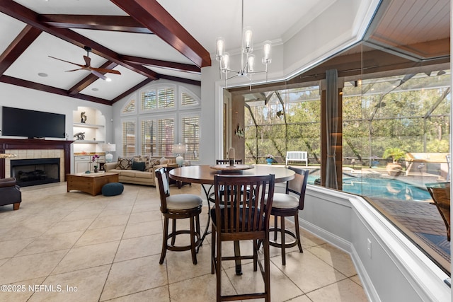 dining room with lofted ceiling with beams, light tile patterned flooring, a tiled fireplace, and ceiling fan with notable chandelier