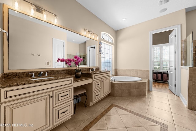 full bathroom with tile patterned flooring, a garden tub, double vanity, and a sink