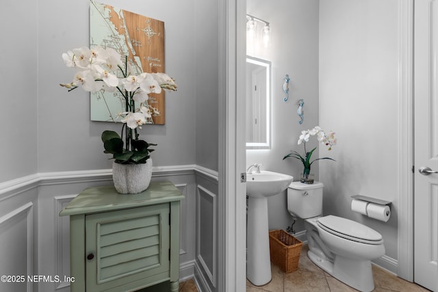 bathroom with a wainscoted wall, toilet, a sink, a decorative wall, and tile patterned flooring