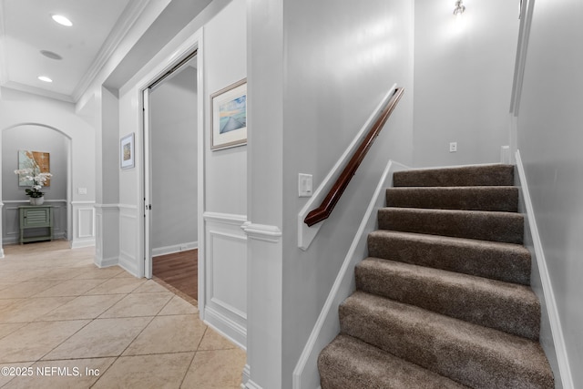 staircase featuring crown molding, recessed lighting, arched walkways, tile patterned floors, and a decorative wall