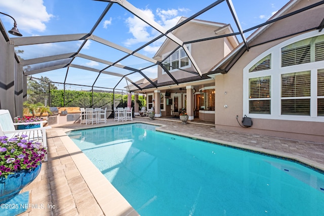 outdoor pool with outdoor dining space, a ceiling fan, glass enclosure, exterior kitchen, and a patio area