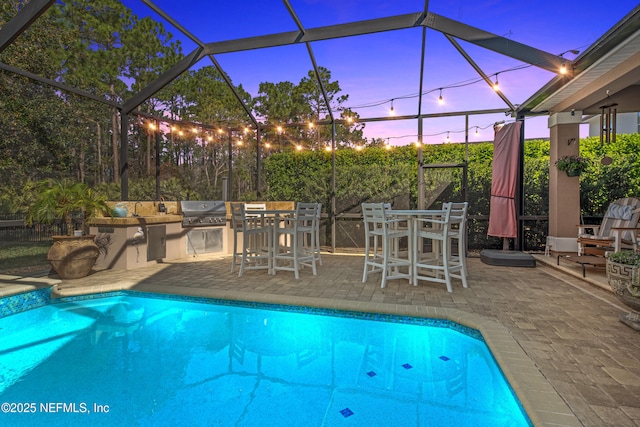 pool at dusk with a lanai, exterior kitchen, outdoor dining area, a patio area, and an outdoor pool