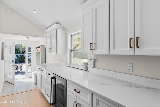 kitchen with wine cooler, lofted ceiling, light stone countertops, and white cabinetry