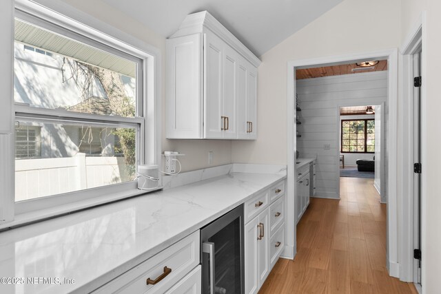 kitchen featuring wine cooler, lofted ceiling, light stone counters, light wood-style floors, and white cabinets