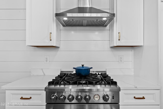 details featuring light stone counters, white cabinets, gas range oven, and wall chimney range hood