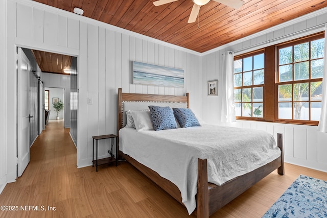 bedroom with a barn door, multiple windows, light wood-type flooring, and wooden ceiling