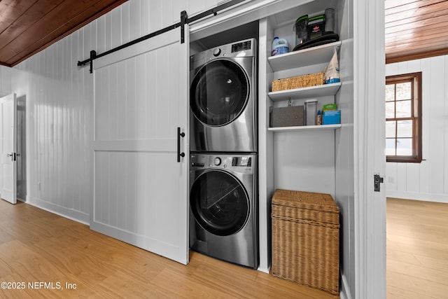 washroom featuring wood ceiling, light wood-type flooring, a barn door, laundry area, and stacked washing maching and dryer