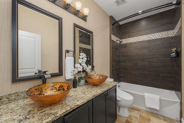 bathroom with a textured ceiling, toilet, a sink, visible vents, and double vanity