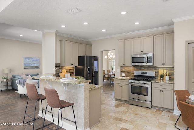 kitchen with appliances with stainless steel finishes, a notable chandelier, a peninsula, and light stone countertops