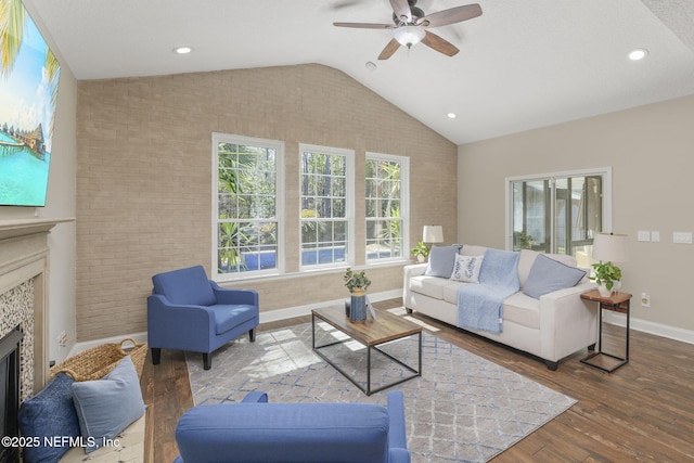 living area with lofted ceiling, a fireplace, brick wall, and wood finished floors