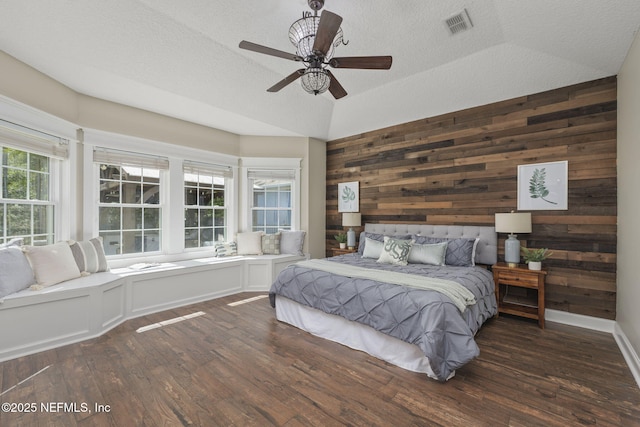 bedroom featuring a textured ceiling, ceiling fan, wood walls, dark wood-style flooring, and visible vents