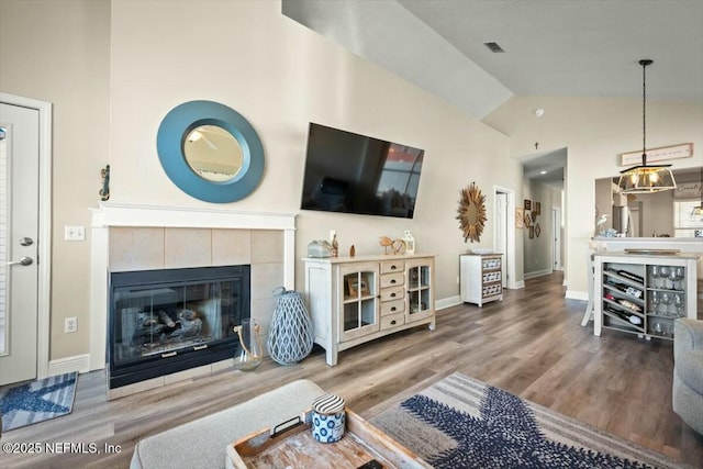 living room with visible vents, a tiled fireplace, wood finished floors, high vaulted ceiling, and baseboards