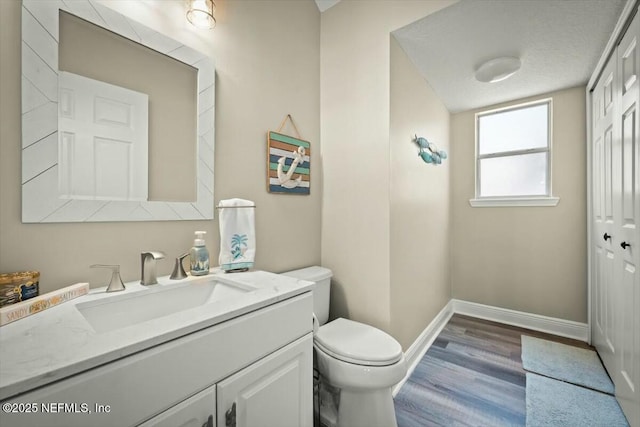 half bath with toilet, baseboards, wood finished floors, and vanity