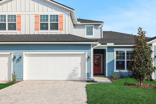 view of front of home featuring roof with shingles, an attached garage, decorative driveway, a front lawn, and board and batten siding