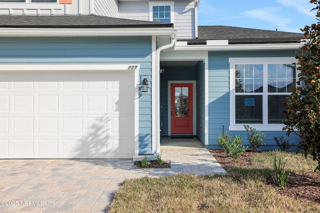 entrance to property featuring a garage, a shingled roof, and decorative driveway