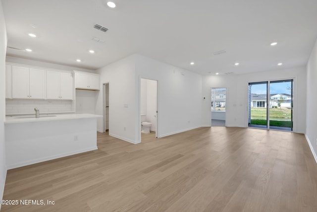 unfurnished living room featuring visible vents, baseboards, light wood-style floors, a sink, and recessed lighting