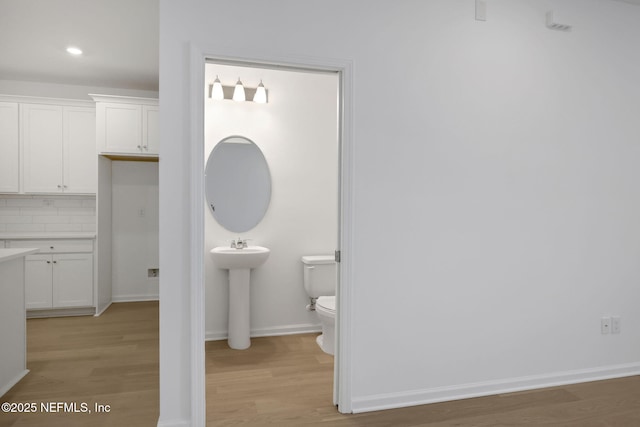 half bath with tasteful backsplash, wood finished floors, toilet, and baseboards