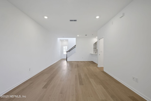 unfurnished living room featuring visible vents, baseboards, light wood-style flooring, stairway, and recessed lighting