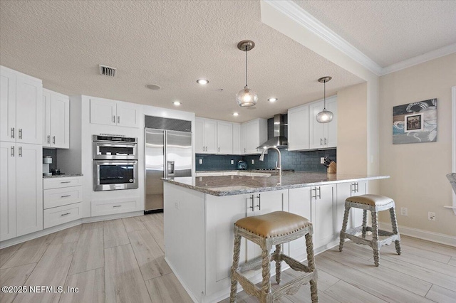 kitchen with a peninsula, wall chimney range hood, a kitchen bar, and stainless steel appliances