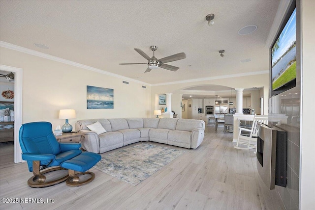 living area featuring arched walkways, a textured ceiling, light wood-type flooring, decorative columns, and crown molding