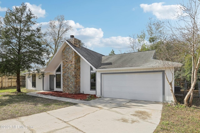 mid-century modern home featuring an attached garage, a shingled roof, fence, concrete driveway, and a chimney