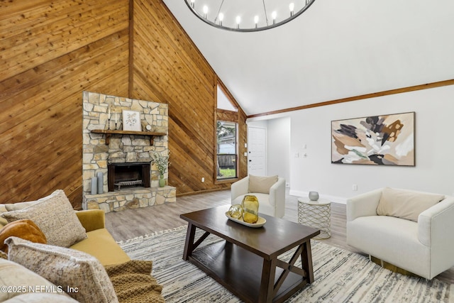 living area with wooden walls, an inviting chandelier, a stone fireplace, light wood-style floors, and high vaulted ceiling