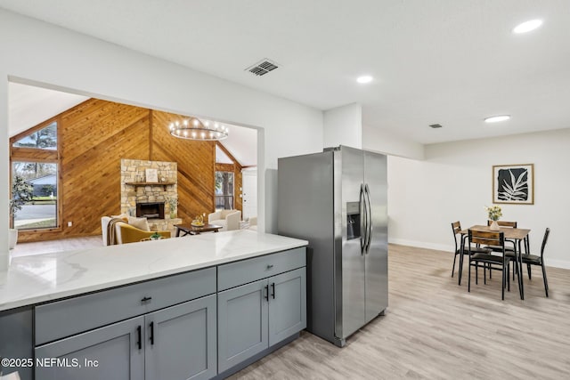 kitchen with light stone counters, gray cabinetry, a fireplace, visible vents, and stainless steel fridge