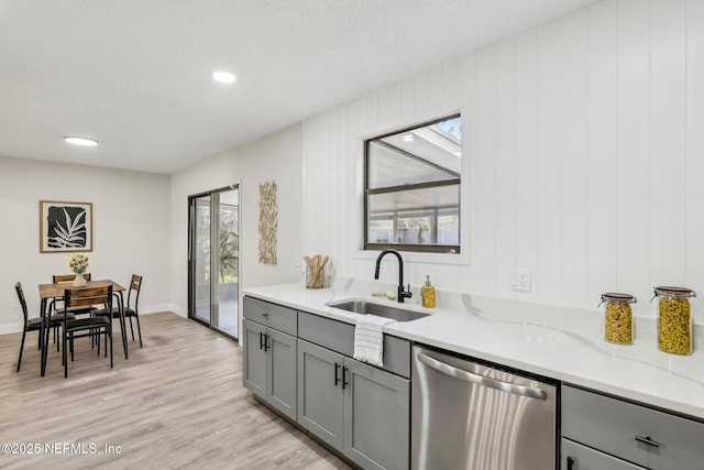 kitchen with light stone counters, gray cabinetry, a sink, light wood-type flooring, and dishwasher