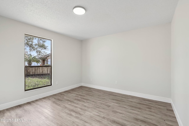 spare room featuring a textured ceiling, baseboards, and wood finished floors