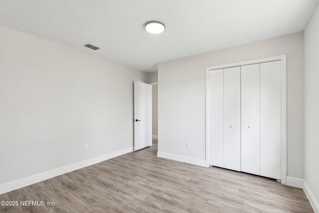 unfurnished bedroom with light wood-style floors, baseboards, visible vents, and a textured ceiling